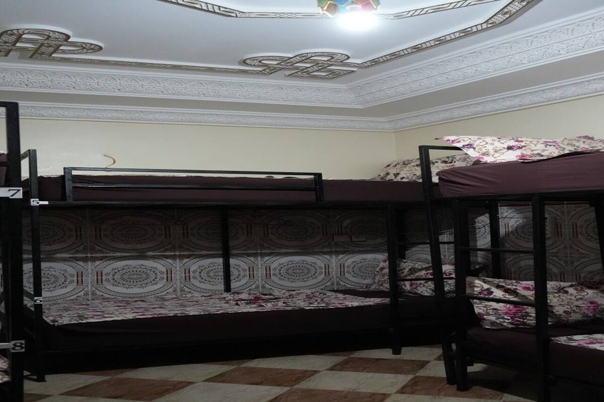 A dormitory room with bunk beds, patterned bedding, and a checkered floor.