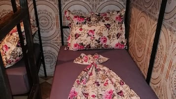 A single bed with a floral bedspread and a matching pillow, a wooden chair, and a patterned wall.