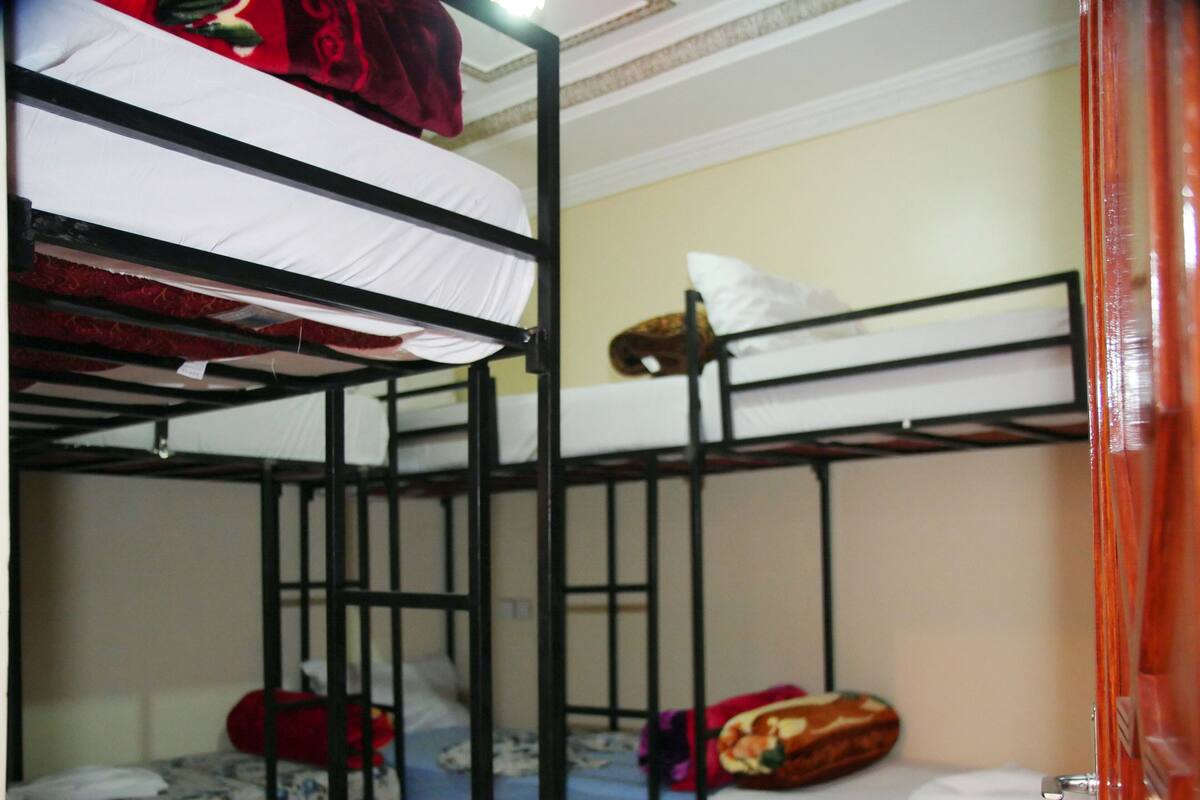 A dormitory room with bunk beds, a wooden wardrobe, and a tiled floor.