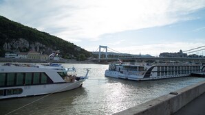 Un río con barcos amarrados, un puente al fondo y edificios a lo largo de la orilla.