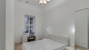 Un dormitorio con cama, escritorio, silla, ventana y candelabro.