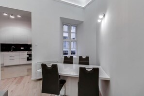Una cocina moderna con armarios blancos y encimera negra, un comedor con mesa blanca y sillas negras, y una ventana con múltiples divisiones.