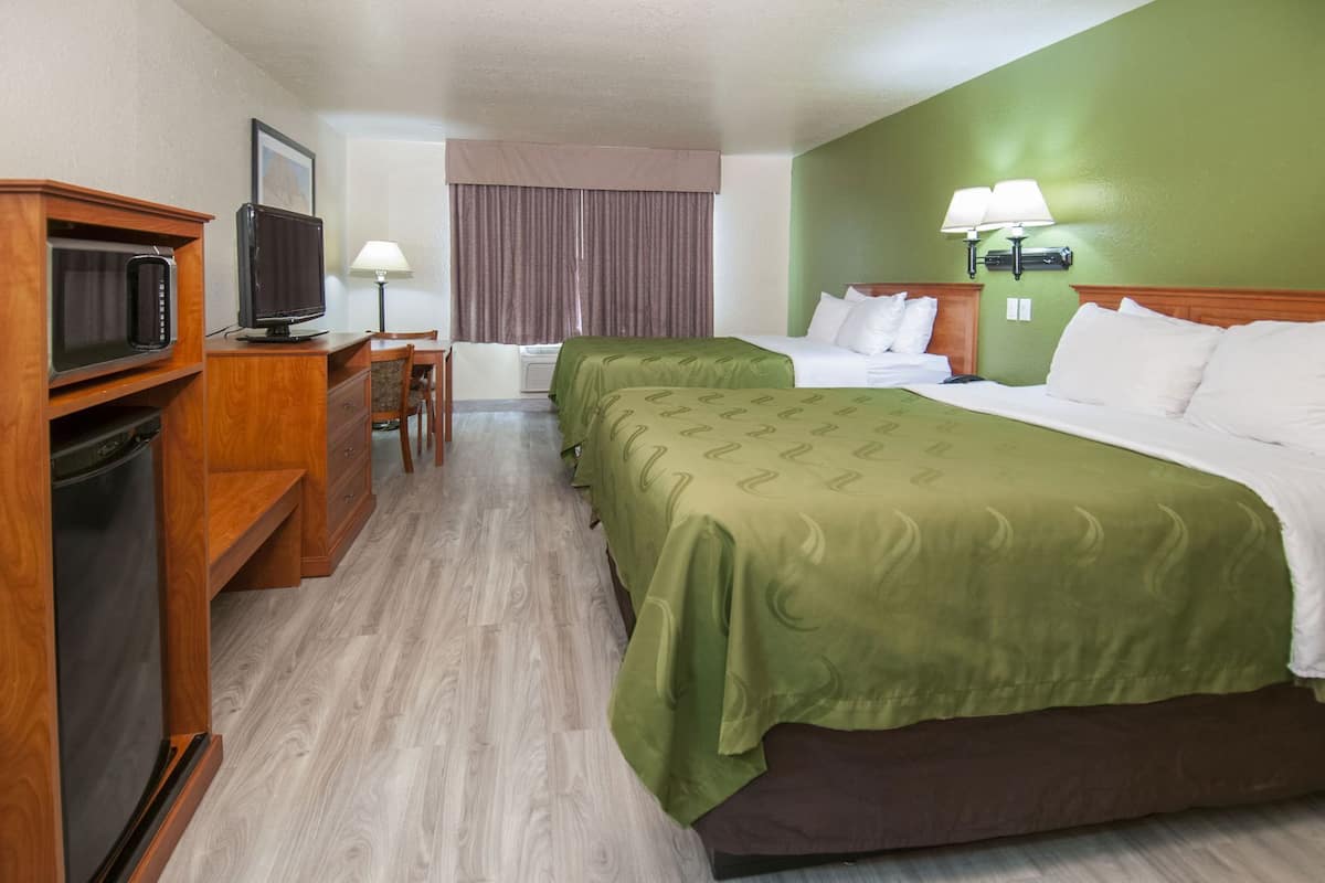 Een hotelkamer met een bed, een bureau met stoel, een televisie en een lamp.
