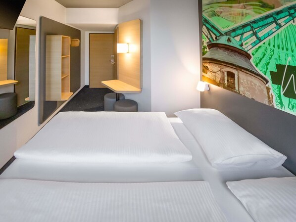 A hotel room with a bed, a small desk, a mirror, and a wall-mounted light. -  B&B HOTEL Würzburg-Ost (Würzburg)