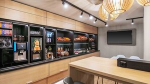A modern kitchen with built-in appliances, a bar area with various food items, and a seating area with chairs. -  B&B HOTEL Würzburg-Ost (Würzburg)
