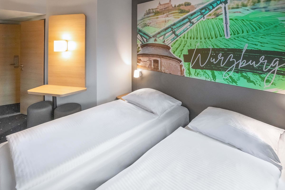 Une chambre d’hôtel avec deux lits, une petite table et une lampe fixée au mur.
