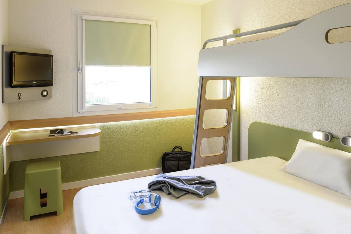 A hotel room with a bunk bed, a desk with a chair, a television, and a window.