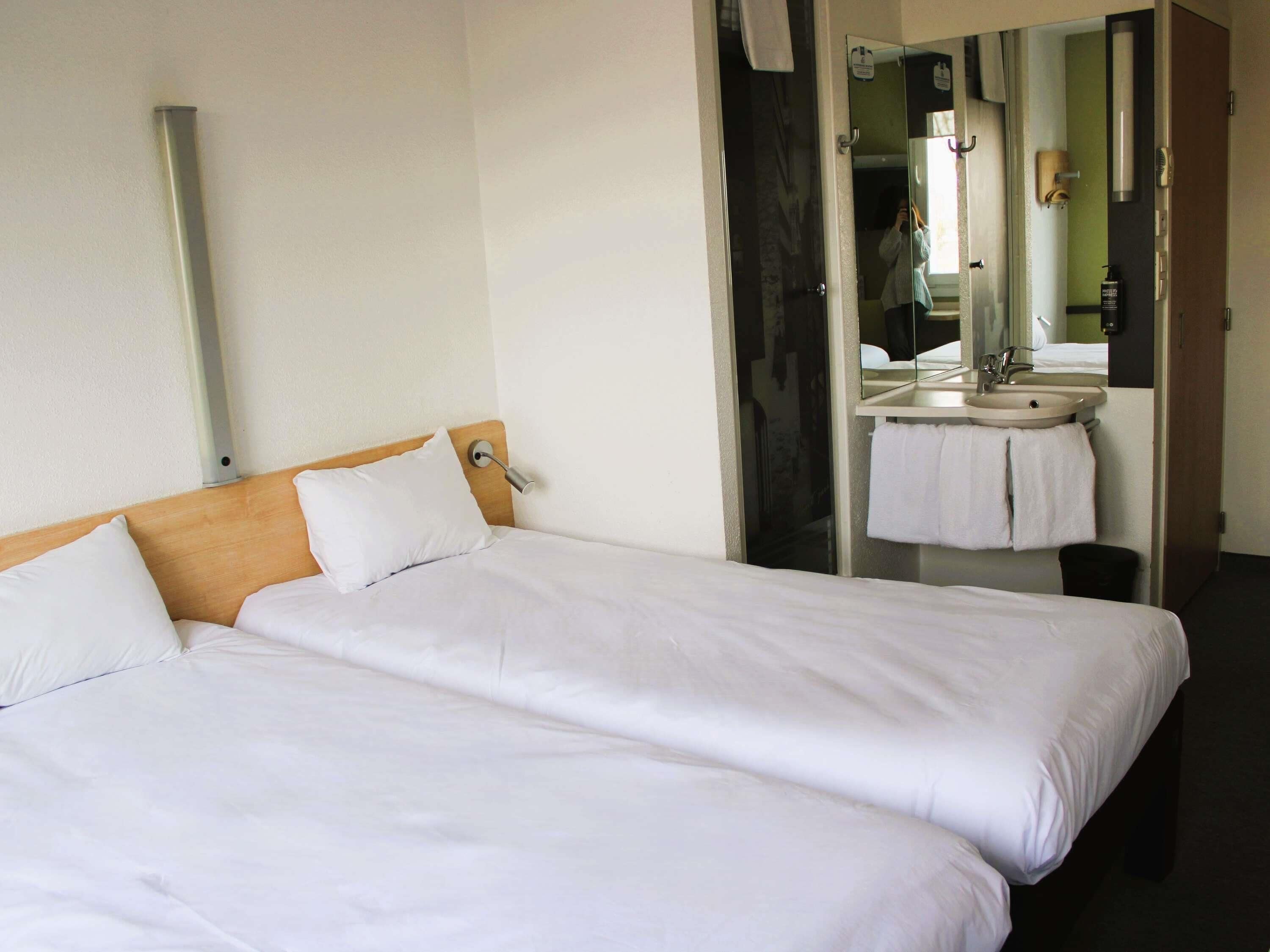 A hotel room with two beds, a bathroom with a sink and mirror, and a door leading to another room.
