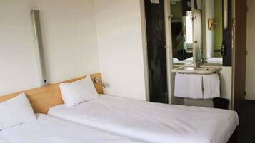 A hotel room with two beds, a bathroom with a sink and mirror, and a door leading to another room.