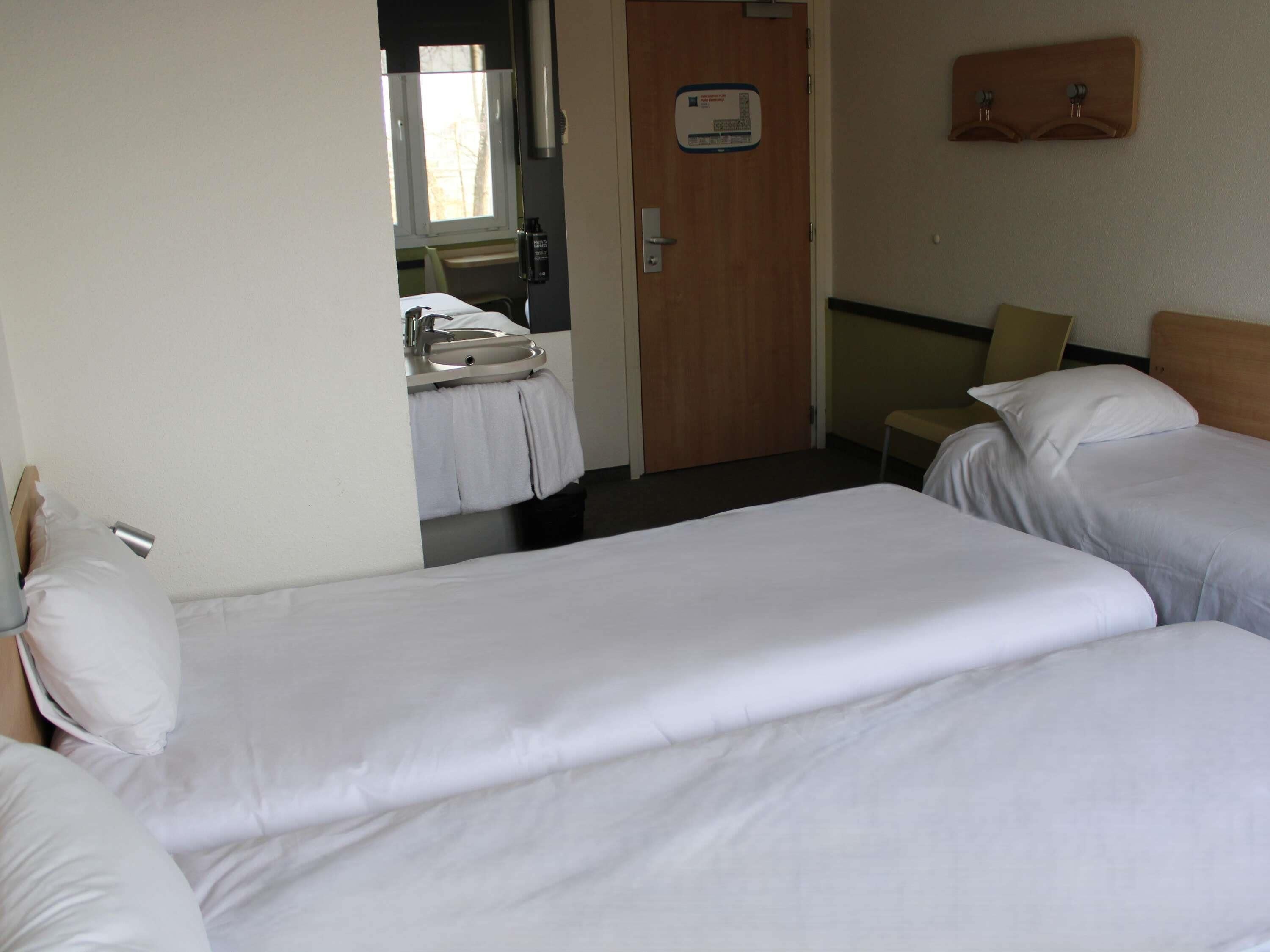 A hotel room with two beds, a bathroom with a sink, and a door with a keypad lock.