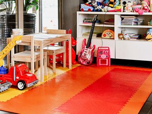 A child's playroom with a wooden table, chairs, a red toy truck, a pink toy guitar, and a bookshelf filled with books and toys. - Ibis Budget Wroclaw Stadion (Wroclaw)