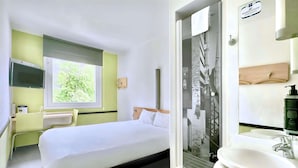 A hotel room with a bed, a window, a shower, and a sink. - Ibis Budget Wroclaw Stadion (Wroclaw)