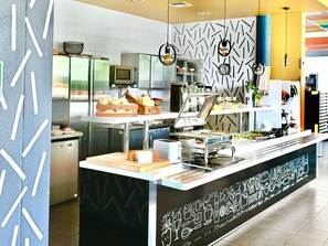 A modern kitchen with stainless steel appliances, a buffet counter, and decorative wall patterns. - Ibis Budget Wroclaw Stadion (Wroclaw)