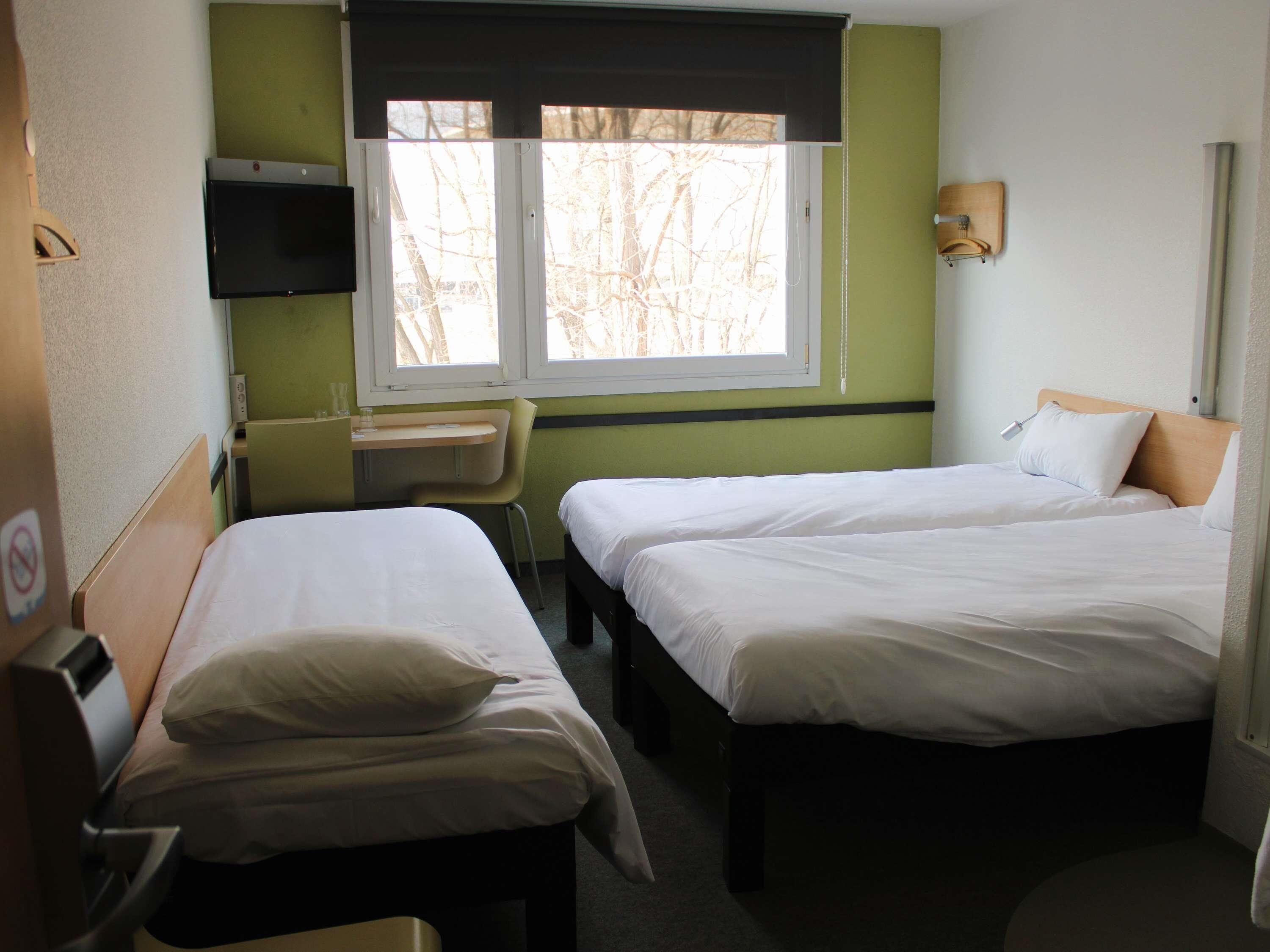 Habitació d'hotel amb dos llits individuals, una taula de treball, una cadira, televisió i finestra amb persianes.