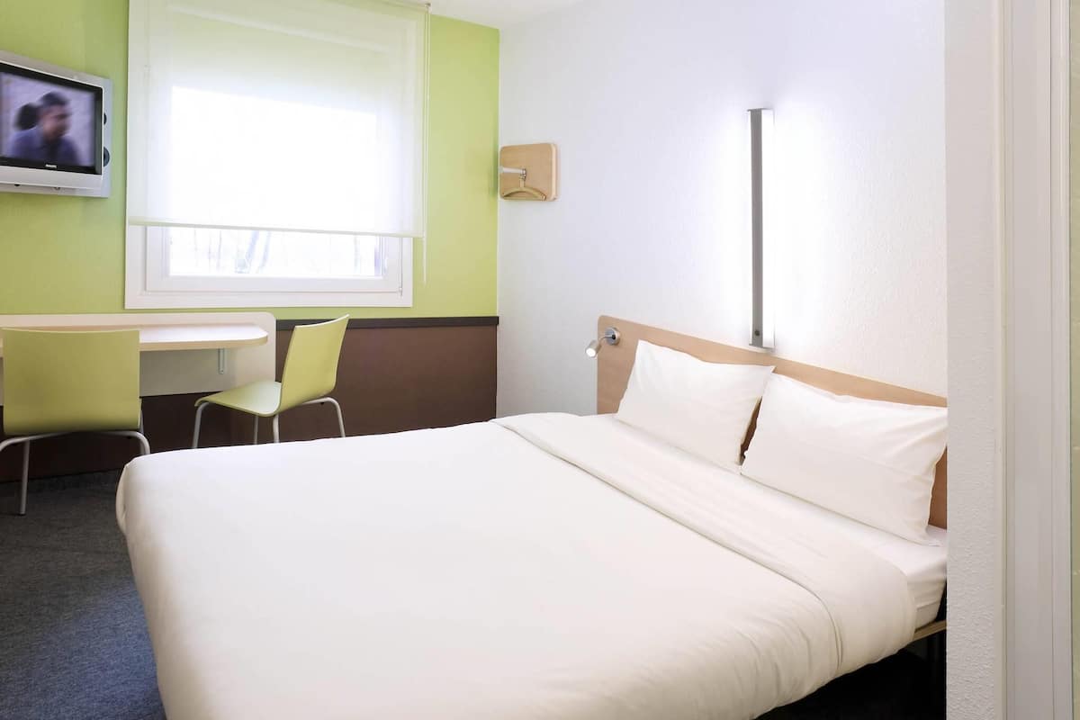 Une chambre d’hôtel avec un lit, un bureau, une chaise, une télévision et une fenêtre.