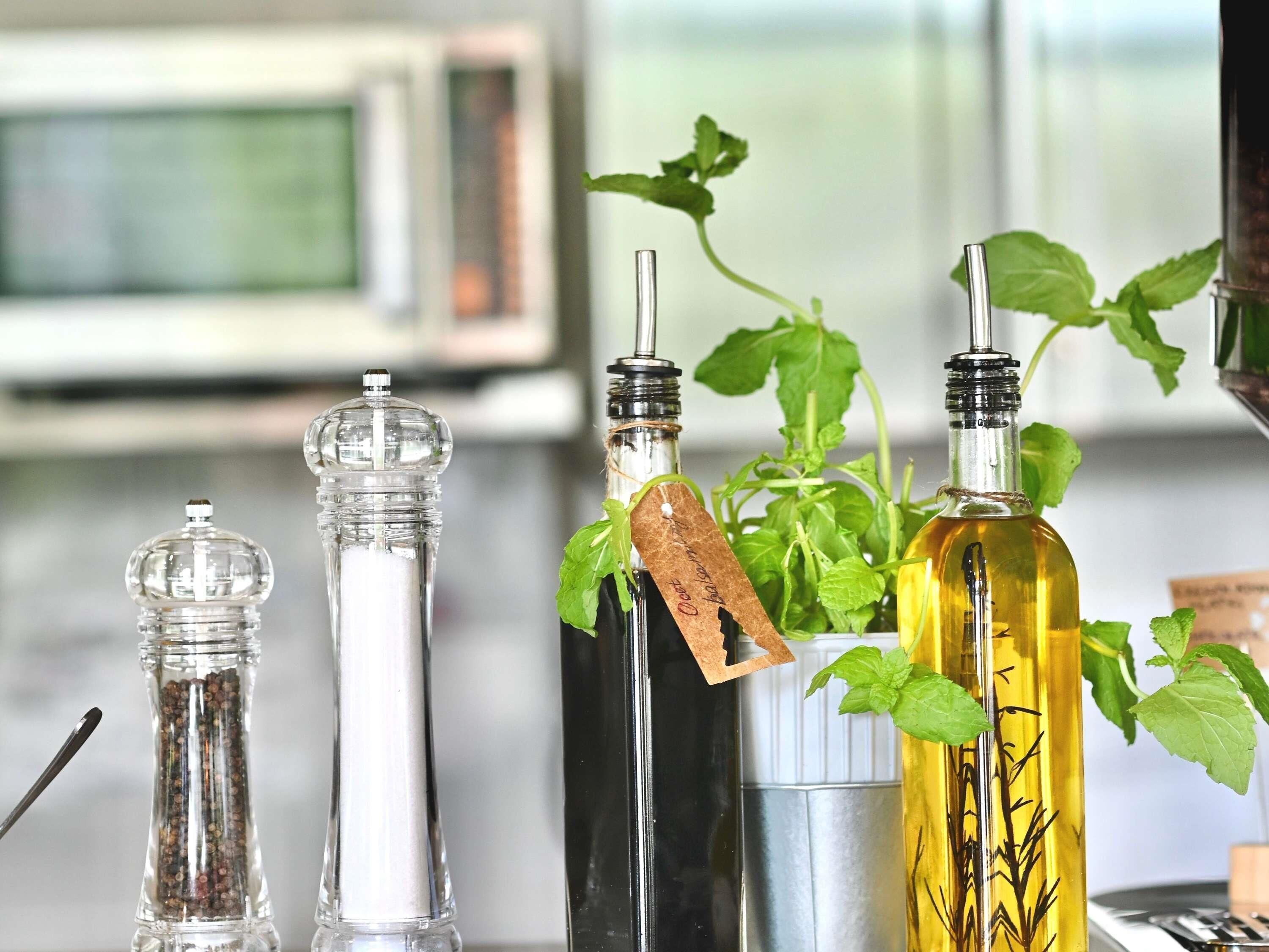 Cuatro botellas de vidrio con etiquetas, un molinillo de pimienta y una planta de menta.