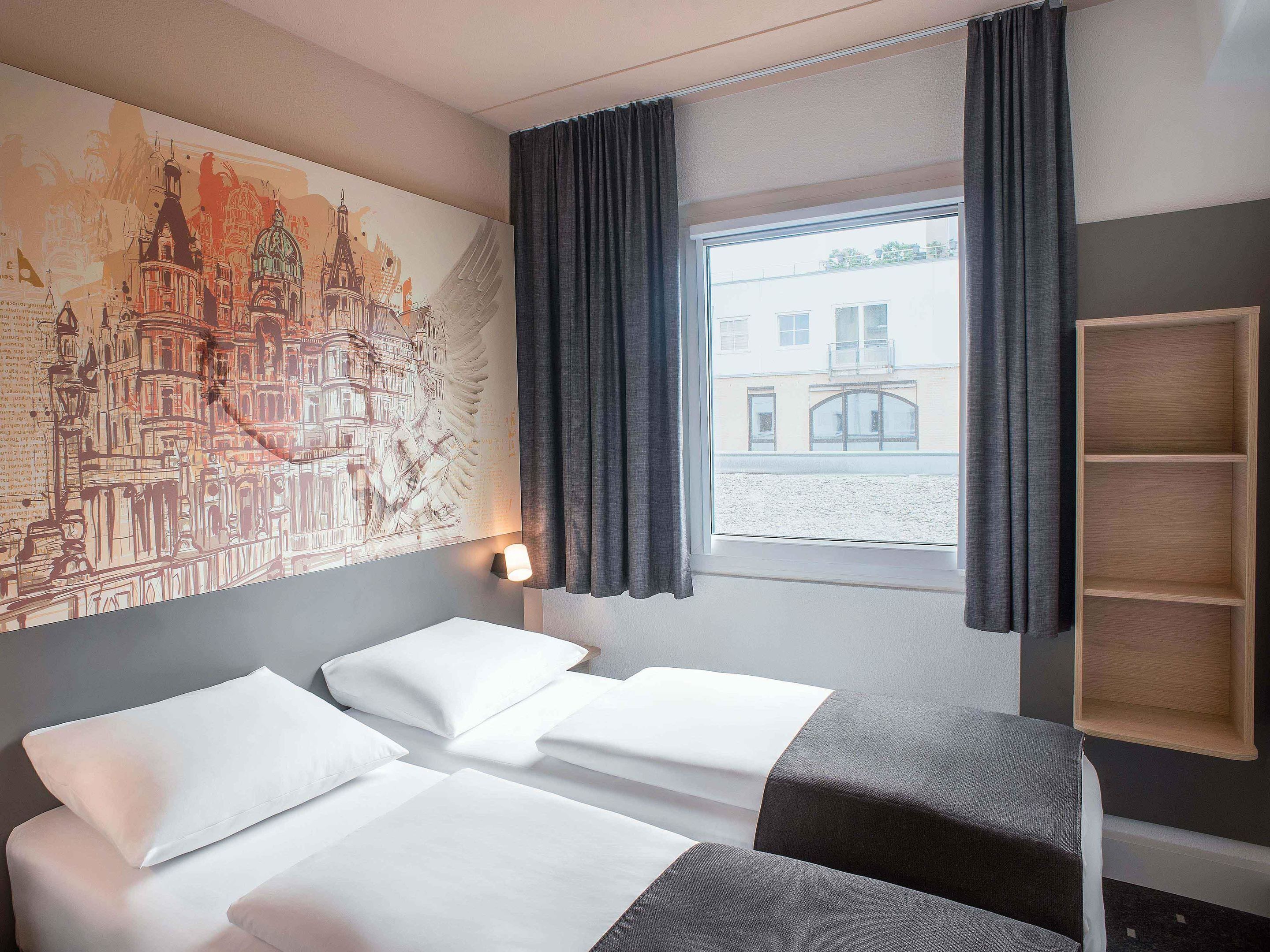 Habitación de hotel con cama, mesita de noche, repisa en la pared y ventana con cortinas.