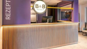 A reception area with a modern design, featuring a reception desk, a sign for B&B Hotels, and a glass partition. - B&B HOTEL Schwerin-Süd (Schwerin)