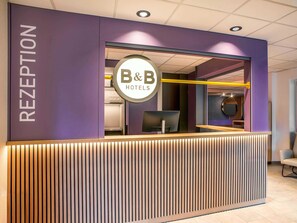 Ein Empfangsbereich mit modernem Design, der einen Empfangstresen, eine Beschilderung für B&B Hotels und eine Glastrennwand zeigt.