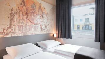 Une chambre d’hôtel avec deux lits, une grande fresque représentant un paysage urbain sur le mur, une fenêtre avec des rideaux et une vue sur les bâtiments à l’extérieur.