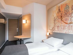 Une chambre d’hôtel avec un lit, un bureau et une lampe fixée au mur.