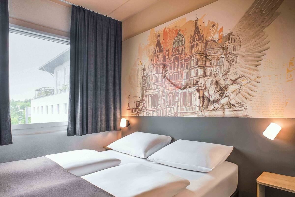 Una habitación de hotel con una cama, un mural grande en la pared y una ventana con cortinas.
