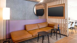 A modern room with a sofa, a small table, a lamp, a TV, and a mirror. - B&B HOTEL Schwerin-Süd (Schwerin)