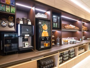 Un bar à petit-déjeuner moderne, équipé d’une machine à café, d’une sélection de thés et d’un présentoir de fruits.