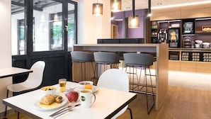 A modern cafe with a white table, chairs, and a breakfast setting including a plate of food, a mug, and a glass of orange juice. - B&B HOTEL Schwerin-Süd (Schwerin)