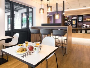 Ein modernes Café mit einem weißen Tisch, Stühlen und einer Frühstücksecke, darunter ein Teller mit Speisen, eine Tasse und ein Glas Orangensaft.