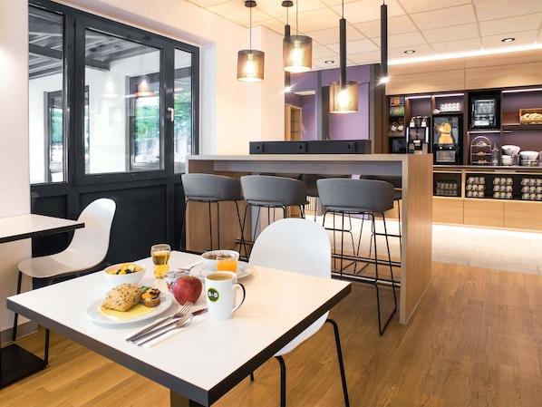 Un café moderno con una mesa blanca, sillas y una mesa lista para el desayuno, que incluye un plato de comida, una taza y un vaso de zumo de naranja.