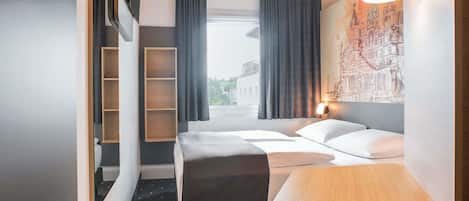 Una habitación de hotel con una cama, una mesita, una silla, una estantería y un cuadro en la pared.
