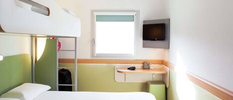 A hotel room with a bunk bed, a bedside table with a camera, a TV mounted on the wall, and a window with a view.