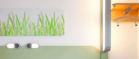 A hotel room with a bed, a headboard with a light green panel, a wall-mounted artwork of grass, and a small shelf with a hook.