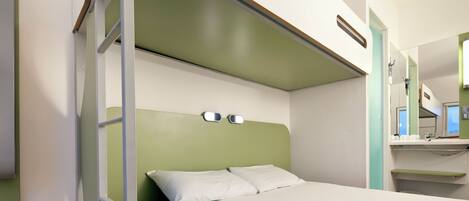 Una habitación de hotel compacta con literas, un escritorio pequeño con espejo y una pared de acento verde.