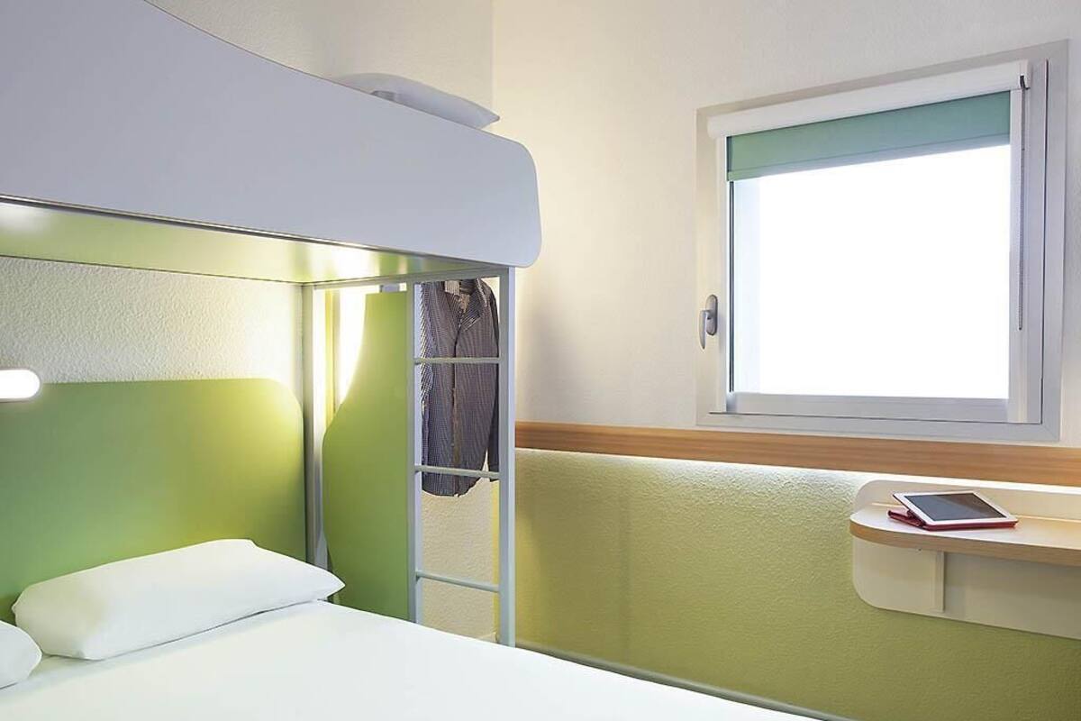 A bunk bed with a green headboard, a bedside table with a tablet, and a window with a view.