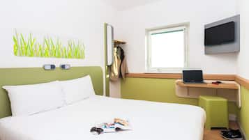A hotel room with a bed, a desk with a laptop, a TV, and a window.