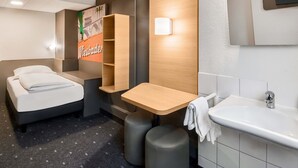 Una habitación de hotel moderna con cama, una mesita, un banco, un lavamanos y un espejo.