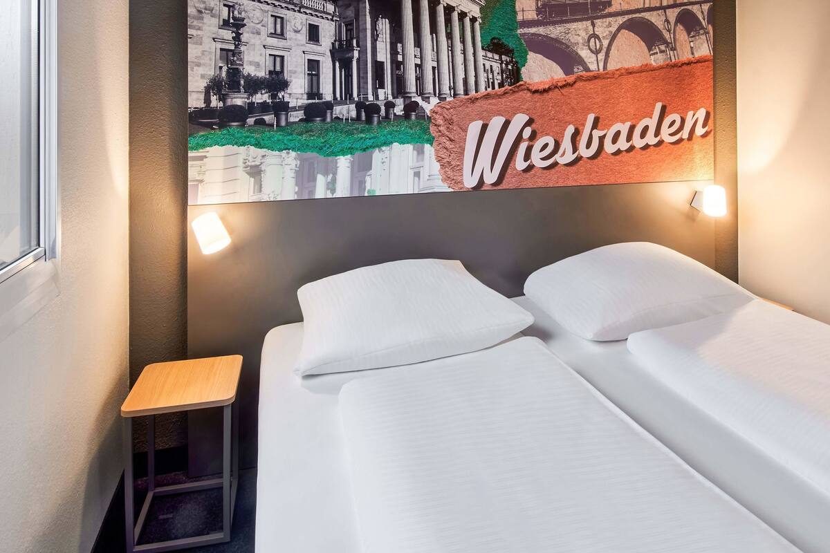 Une chambre d’hôtel avec un lit, une table de chevet et une enseigne fixée au mur sur laquelle on peut lire « Wiesbaden ».