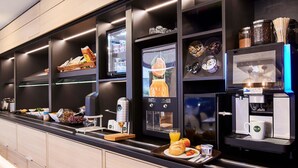 Una barra de desayuno moderna con una máquina de café, diversos alimentos y una exhibición de frutas.