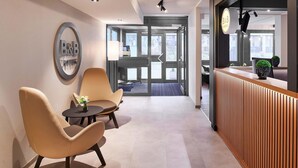 Un moderno vestíbulo de hotel con una mesa de recepción, zona de estar y un gran ventanal que da al exterior.