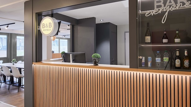 Un área de recepción de hotel moderna con un mostrador de madera, una vitrina con bebidas embotelladas y un letrero que dice "B&B Hotels".