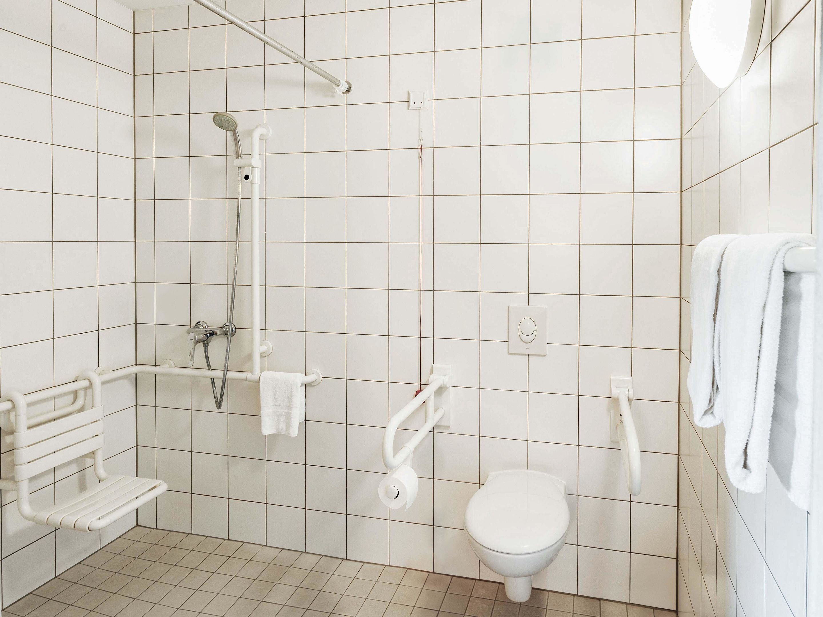 A small, white bathroom with a shower, toilet, and a bench.