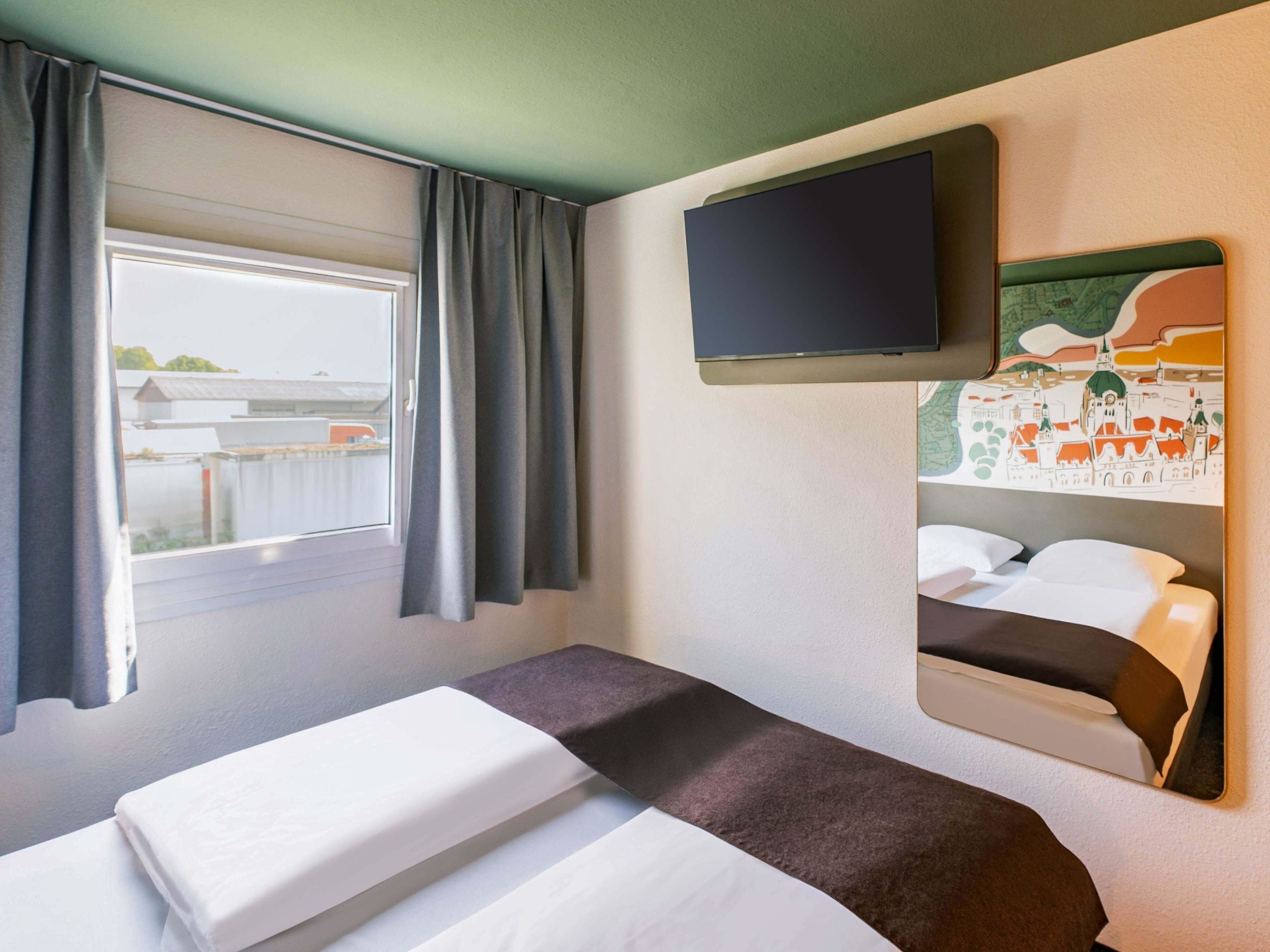 Ein Hotelzimmer mit Bett, Wandfernseher und einem Vorhangfenster.