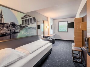Een hotelkamer met een bed, een bureau, een spiegel, een raam en een muur met een stadsgezichtsmural.