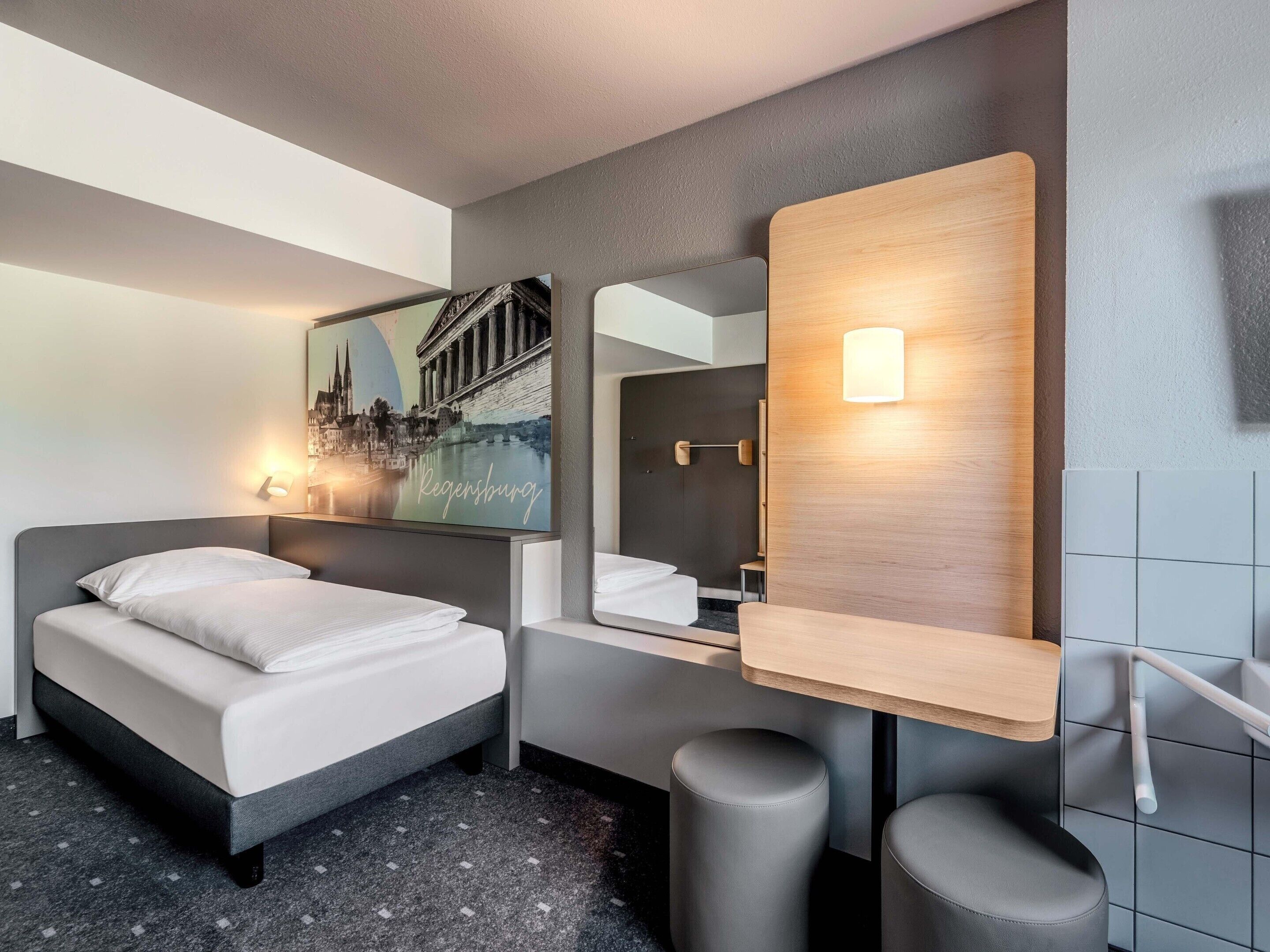 Ein modernes Hotelzimmer mit einem Bett, einem Spiegel, einer Wandleuchte und einem Stadtbild.