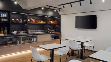 Ein moderner Essbereich mit weißen Stühlen und Tischen, ein Buffet mit verschiedenen Speisen und ein Flachbildfernseher an der Wand.