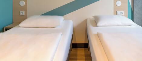 A hotel room with two single beds, a wooden floor, and a teal accent wall.