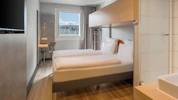 Una habitación de hotel moderna con una cama grande, un escritorio y un ventanal con vistas a edificios.