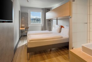Camera d'hotel moderna con un letto grande, una scrivania e una finestra con vista sugli edifici.